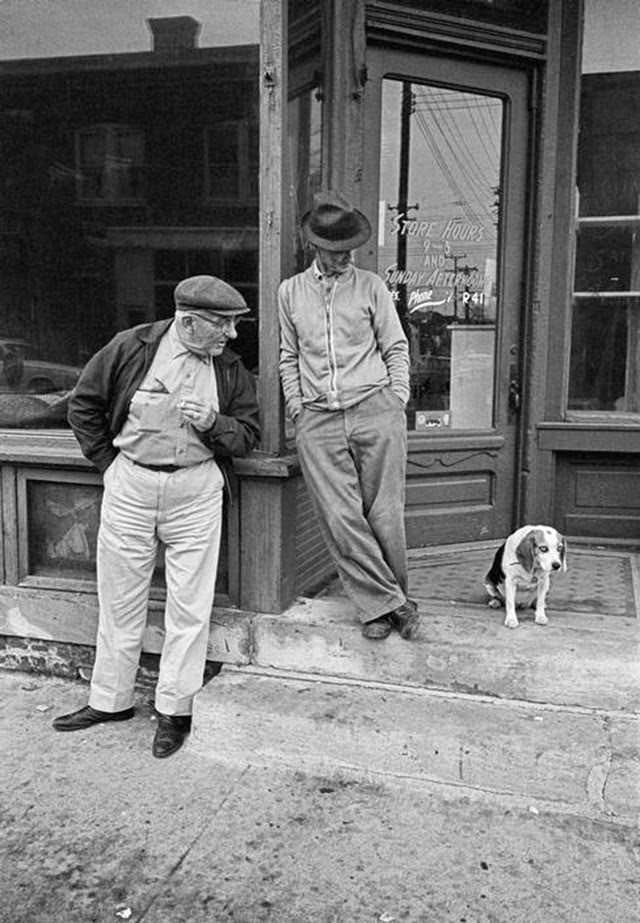 Two men and a dog in front of a small-town storefront in Iowa, 1963