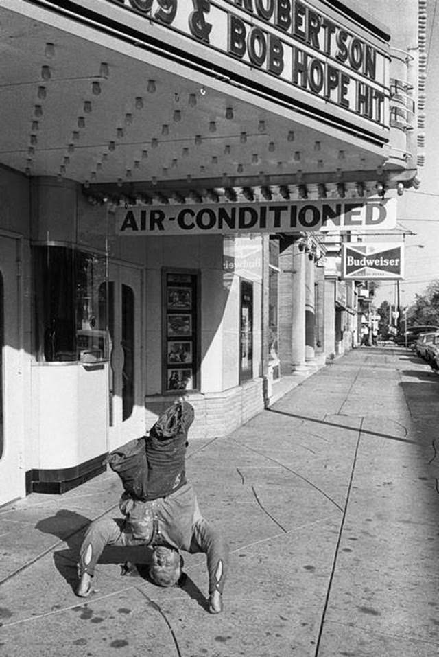Amputee beggar performing a headstand in front of a movie house in Quincy, Illinois, 1963