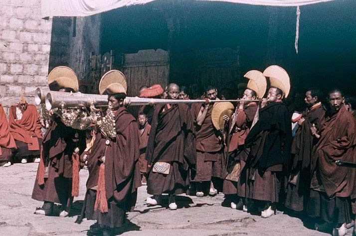 Cheeks ballooning, monks force sirenlike blasts from silver trumpets as they clear the way for their king.