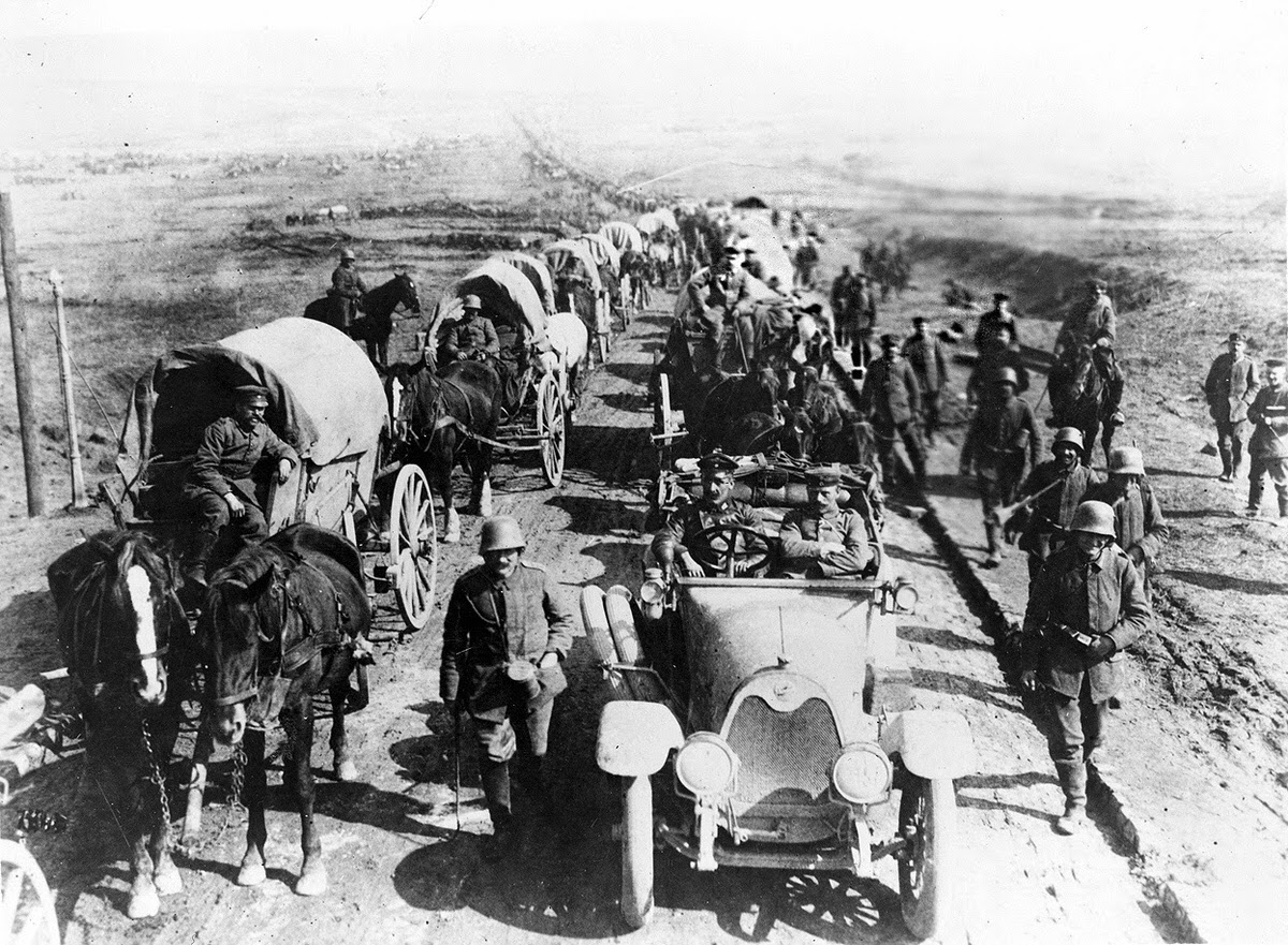 German officers in an automobile with a convoy of wagons and soldiers, 1914