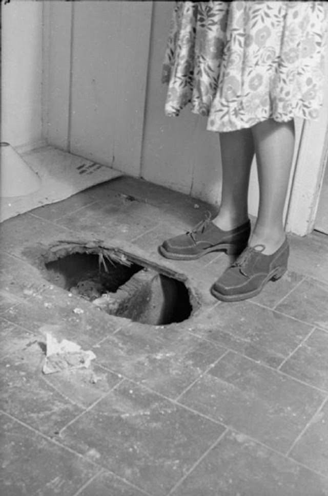 Mrs Day stands alongside a hole in the floor which was made by a fire bomb before the fire was brought under control. This area of the house does not have asbestos sheeting on the floor.