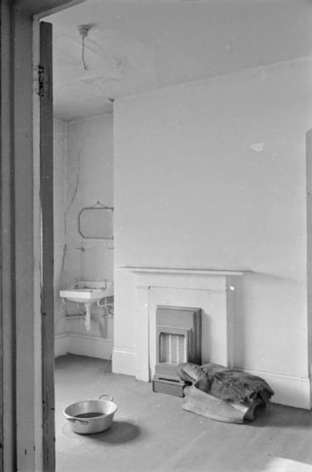 The top floor of Mrs Day’s South Kensington home is no longer in use. Here we see an empty room with a bowl on the floor to catch any drips of rain water that may come in through the bomb-damaged ceiling.