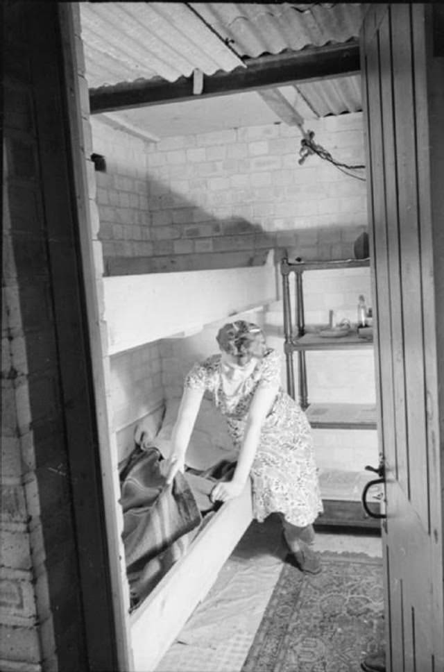 Mrs Day makes up a bunk in the air raid shelter in the cellar of her South Kensington home. The bunks are kept ready in case any night raids force her to spend the night in the shelter. The bunk will hopefully mean that she spends the night in some comfort!