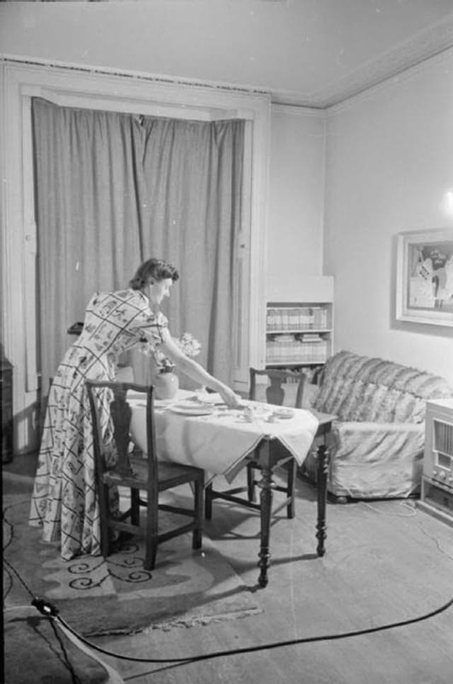 Mrs Day sets the table in preparation for the evening meal in the sitting room of her South Kensington home. She is expecting her naval husband Lt Kenneth Day to arrive home on leave, so the table is set for two and a vase of flowers has been added.