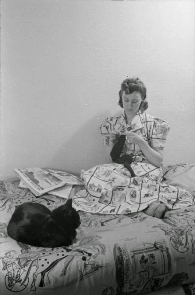 While her evening meal is cooking, Mrs Day settles down on her bed with the evening paper and a spot of sewing. She is working on a balaclava and is accompanied by her cat ‘Little One’.