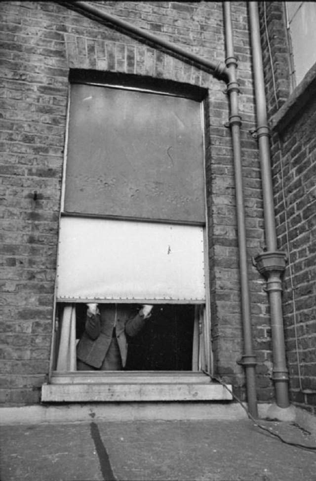 Mrs Day opens her window to let some air, and light, into her South Kensington home. The window panes have been replaced by oiled linen stretched over the frame, as the glass was knocked out by a nearby bomb a short while ago.