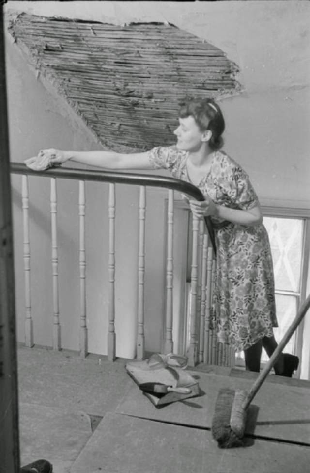 Mrs Day spends half an hour or so on the housework before she leaves for work. Here we see her polishing the bannisters. Above her head, we can see a large patch of missing plaster on the ceiling, caused by a nearby air raid.