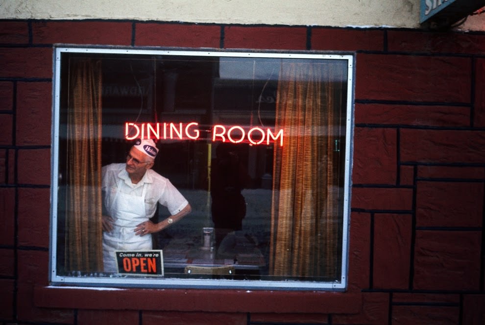 The cook at the Texan Cafe watches the snow removal crew at work, Rifle, Colorado, 1973