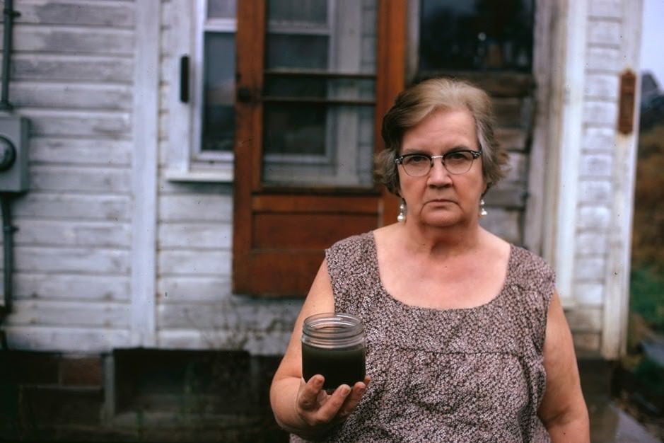 Mary Workman holds a jar of undrinkable water that comes from her well, and she has filed a damage suit against the Hanna Coal Company. She has to transport water from a well many miles away although the coal company owns all the land around her, and many roads are closed, she refuses to sell, near Steubenville, Ohio, 1973