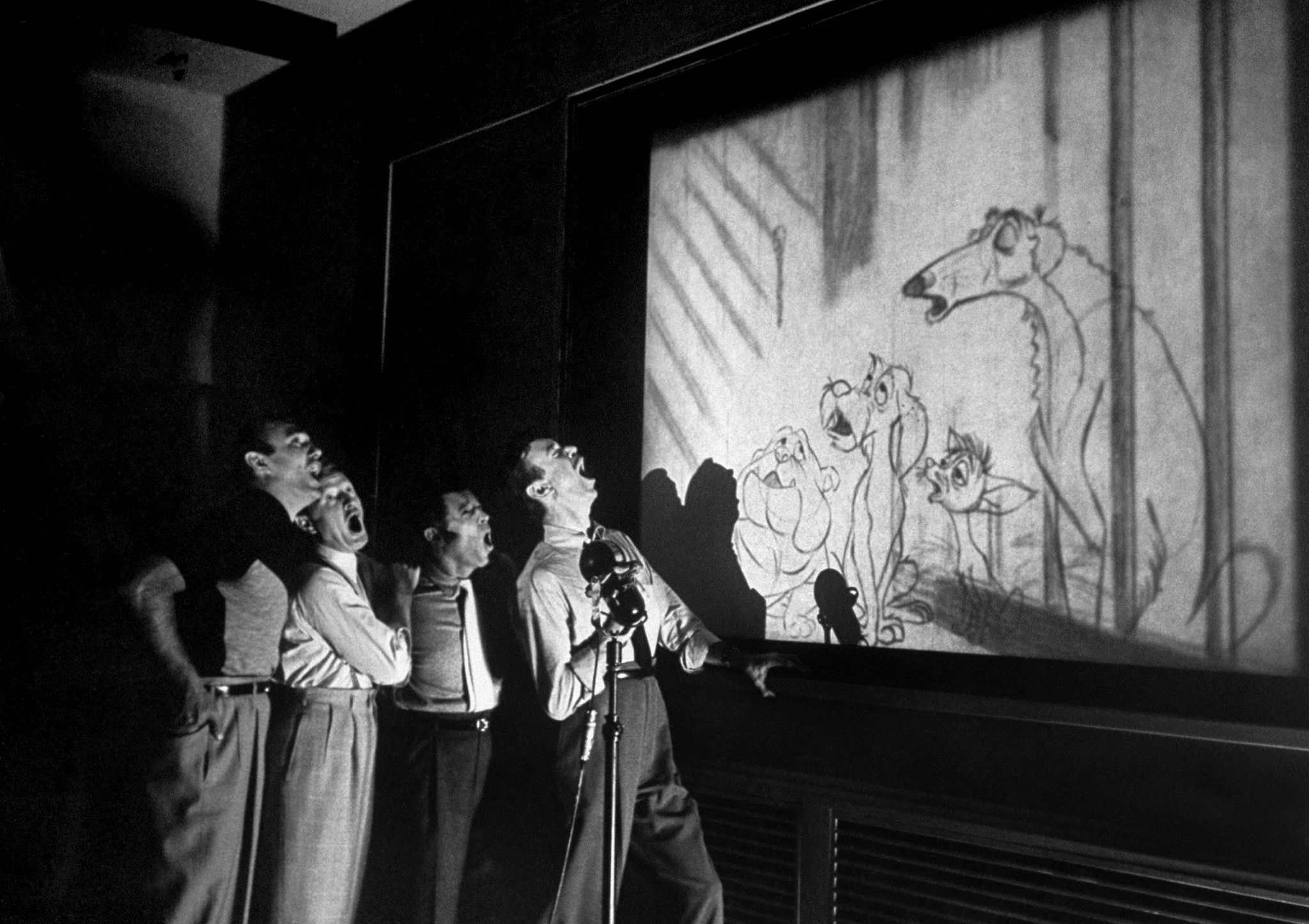 Quartet known as The Mello-Men bays in harmony before screen showing four canine characters whose voices they represent in the forthcoming Disney feature cartoon, The Lady and The Tramp, 1950s