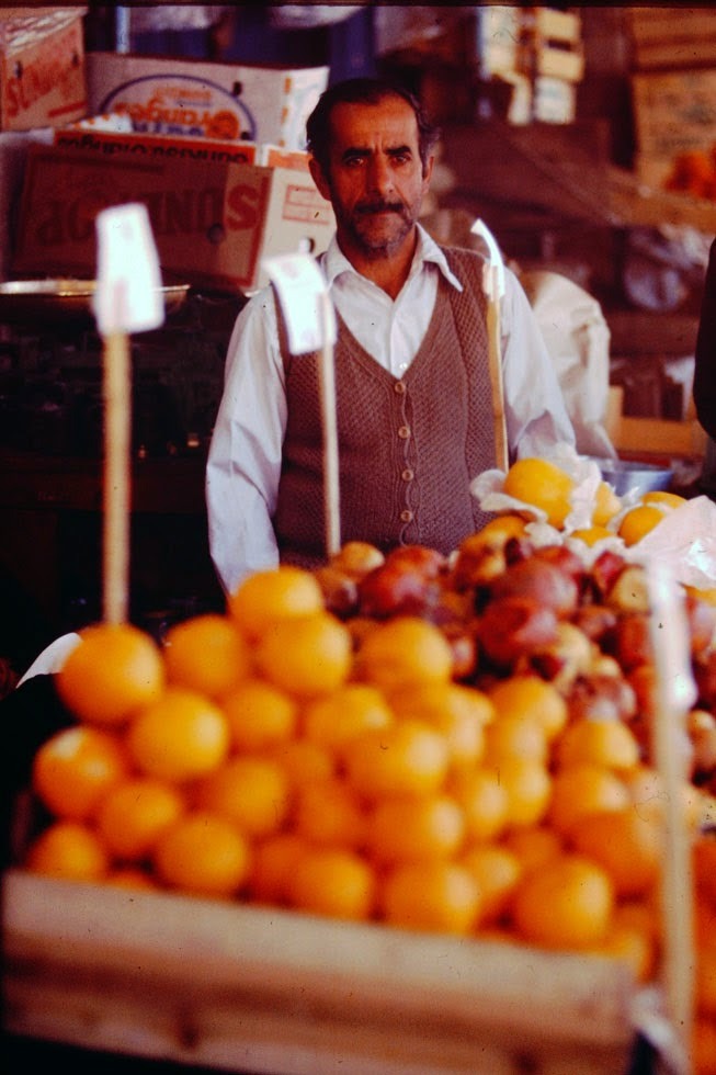 At the fruit market with pomegranates and oranges, probably imported from Israel and Valencia.