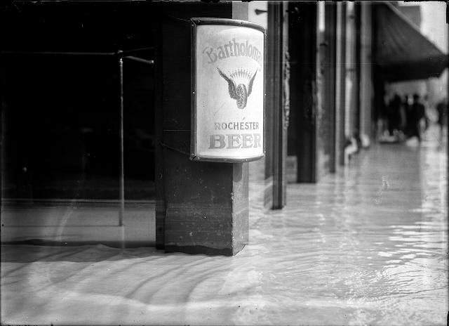 Flood water going into the shops on Front Street. There is a Bartholomay Beer sign on the post, 1913