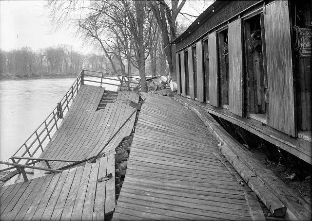 The Durand boathouse in Genesee Valley Park shows major flood damage. The Genesee River, again peaceful, flows past it, 1913