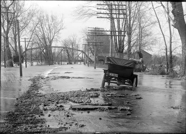 A man leans out of a car to observe the damage done on River Road, 1913