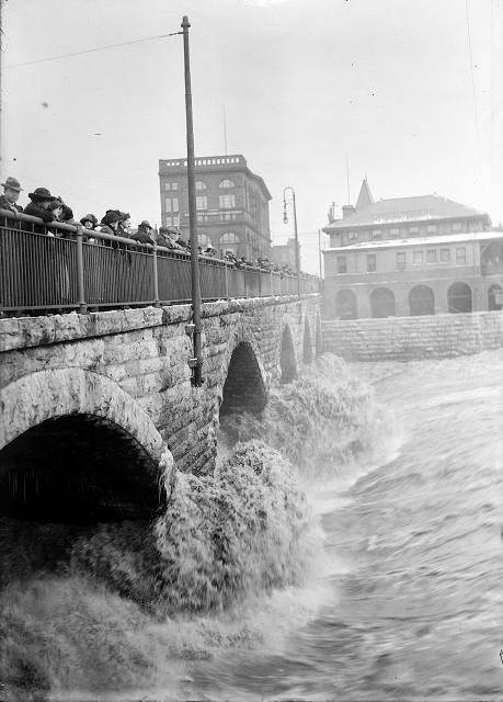 Spectators line the Court Street Bridge railings to watch flood waters beating against the arches of the bridge, below the dam, 1913