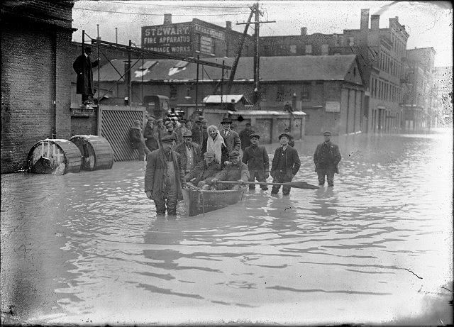 Members of a rescue crew that has saved a woman from a flooded building in and around a rowboat in the middle of flooded Front Street. All records for high water were broken in this flood, 1913