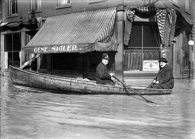 A Front Street policeman patrols his beat in a rowboat during the flood. He and another man row past the Hotel Richmond at the corner of Front and Market Streets, 1913