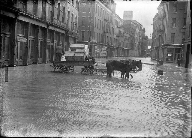 A horse and wagon stand in the middle of Mill Street during the flood. This is Mill Street at Andrews Street. Rochester Thread Company, F.A. Sherwood Company, John M. Forster Company, and Fahy Market are visible, 1913