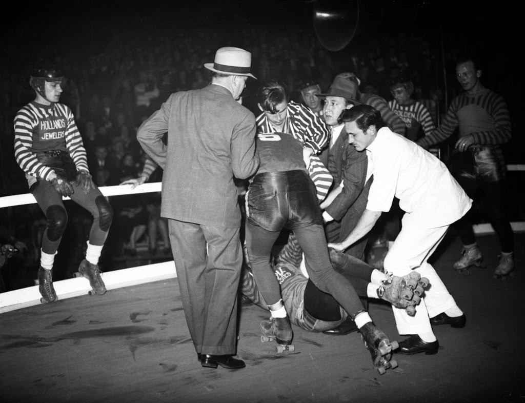 Louis Stasiuk of the New York roller derby team and Paul Gorski of the Chicago roller derby team tangle and spill, then start to fight with Chicagoan Johnny Rosasco joining the fight during the sixth annual roller derby that opened at the Coliseum, 1940s
