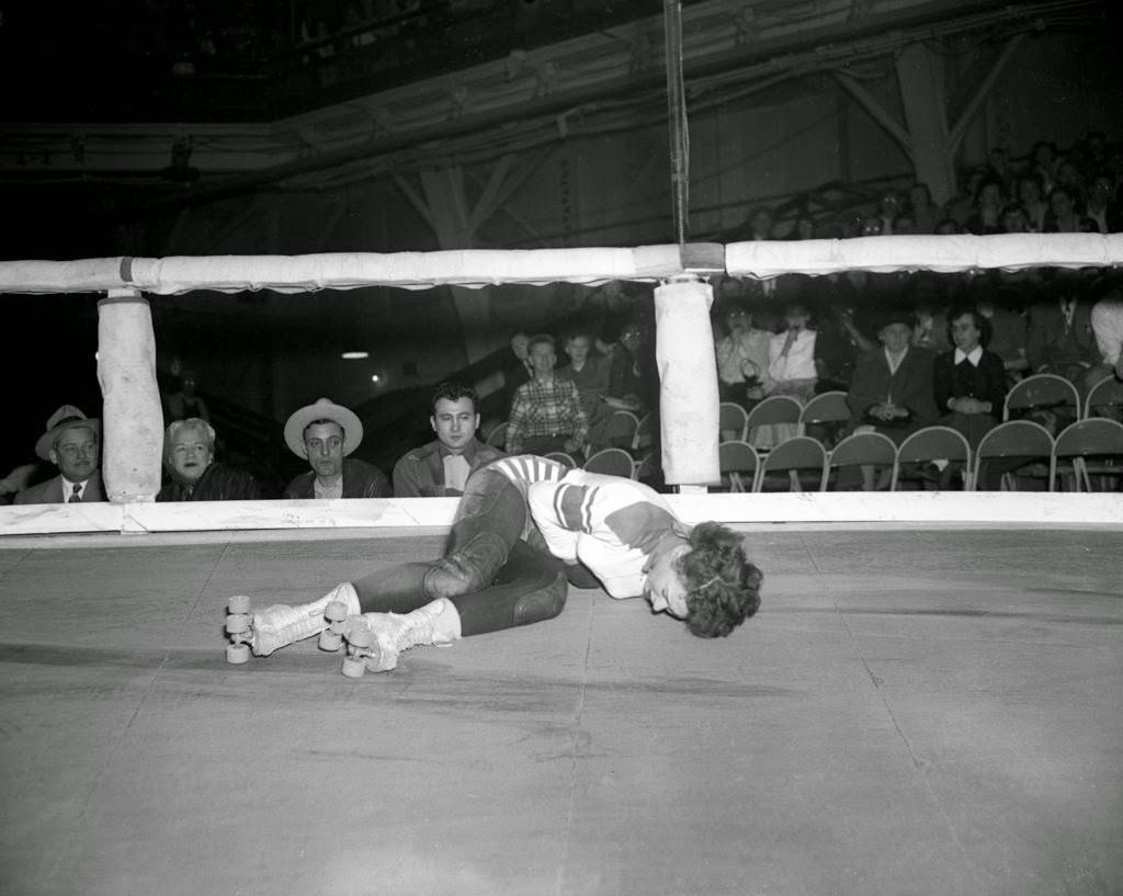 Virginia Rushing from Oklahoma City doubles over in pain after receiving a belt in the midsection during a roller derby at the Coliseum, 1950s