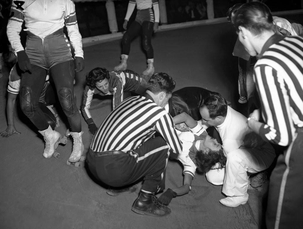 A referee and a doctor aid Betty Boyd of the Jersey Jolters, who was knocked out in a fall during a roller derby at the Coliseum, 1950s